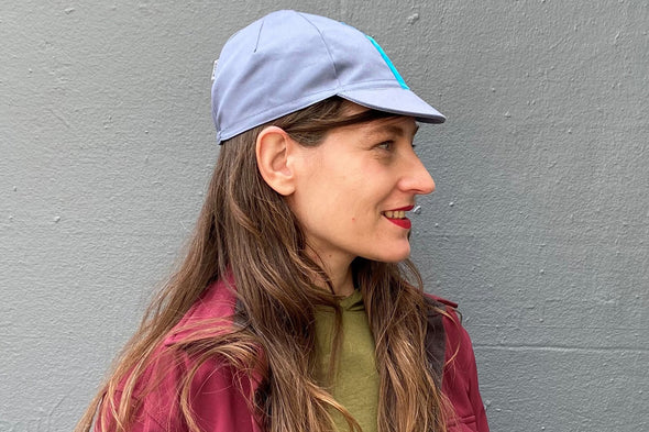 Muriel is wearing the 4-panel cotton cap in blue-grey with a cyan ribbon